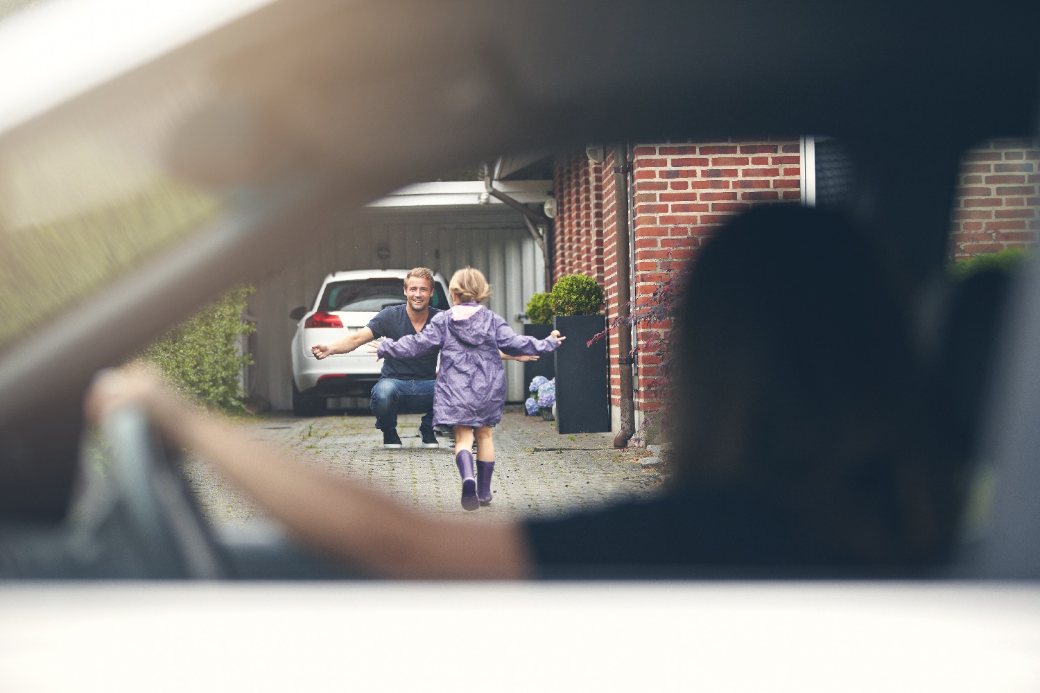 Gjensynsglede mellom far og datter når hun løper ut av bilen. Bildet er tatt gjennom sideruten på mor's hvite bil.